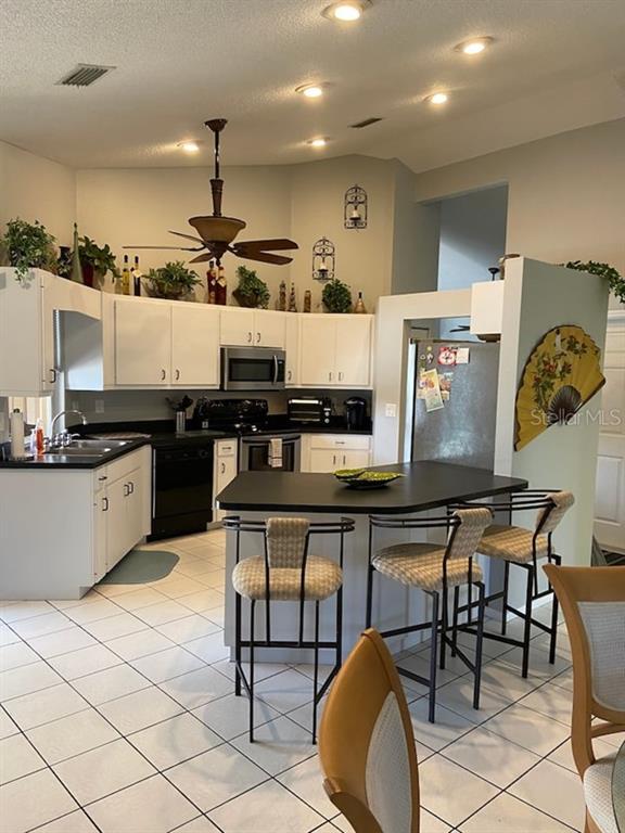A kitchen features white cabinets, black countertops, a central island with bar stools, and tile flooring — 3645 SLAYTON AVENUE, NORTH PORT, FL