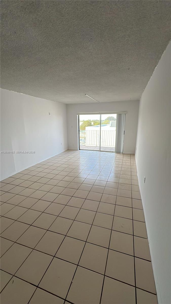 An empty living room features beige tile flooring, white walls, and a sliding glass balcony door — 4480 Palm Ave # 402, Hialeah FL 33012, HIALEAH, FL