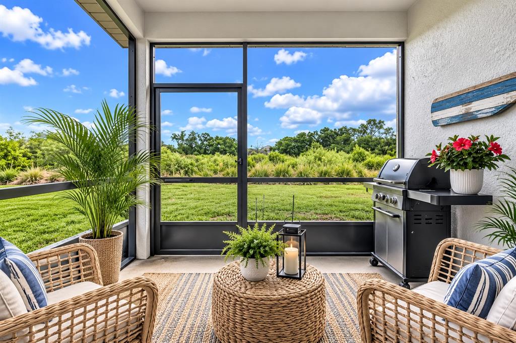 A screened-in patio features wicker furniture, a grill, and a view of a grassy field — 10616 HIGH NOON TRAIL, PARRISH, FL
