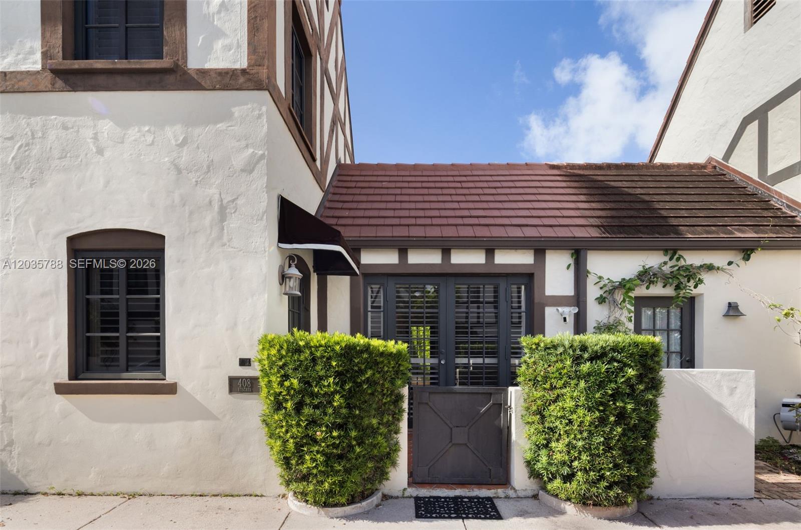The exterior of a stucco home features a gated courtyard entrance and dark-framed windows — 408 Viscaya Ave, Coral Gables FL 33134, CORAL GABLES, FL