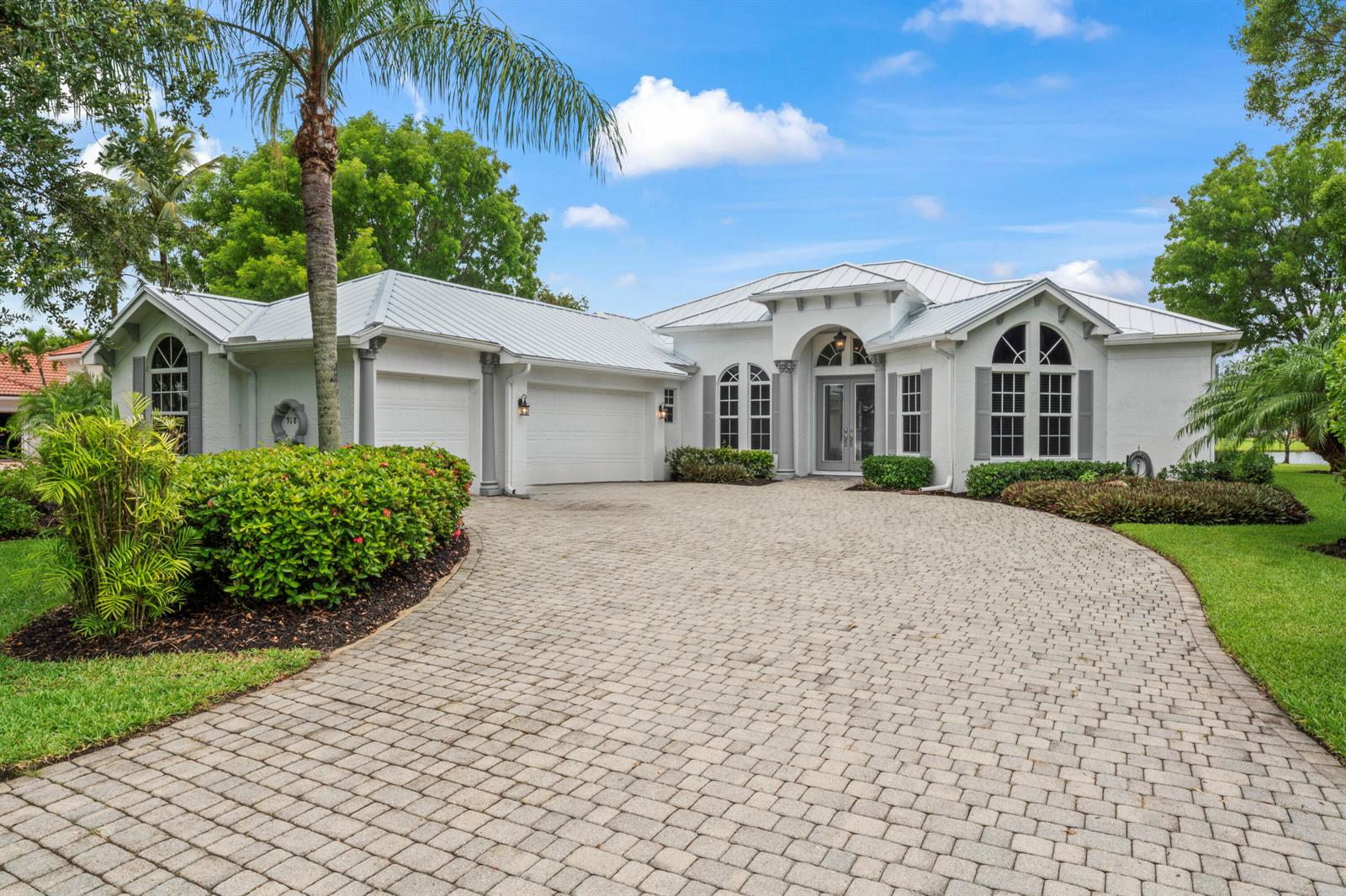 A white single-story house with a metal roof and a paved driveway sits on a lawn — 918 SW Blue Stem Way, Stuart FL 34997, STUART, FL