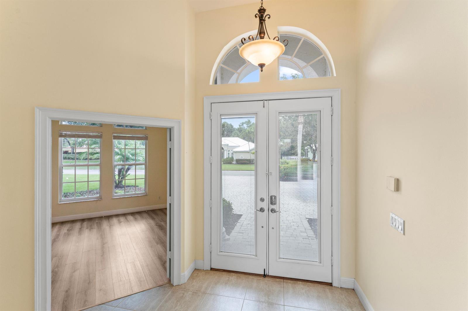 An entryway features double glass doors, a transom window, a chandelier, and tile flooring — 918 SW Blue Stem Way, Stuart FL 34997, STUART, FL