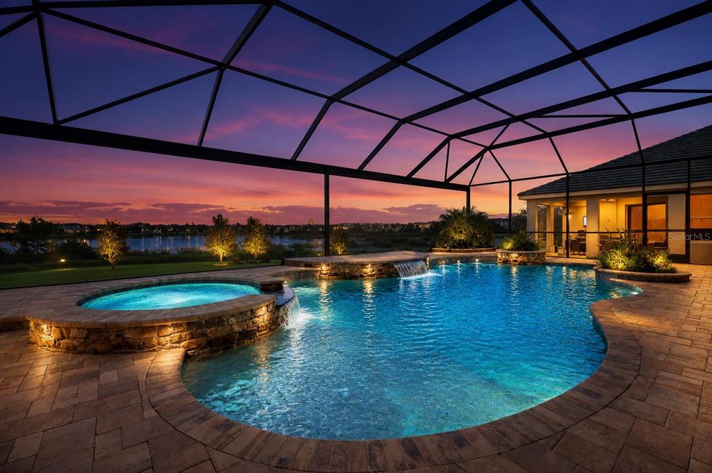 A swimming pool and hot tub with stone accents sit inside a screened-in patio area — 9969 LOST CREEK DRIVE, WINTER GARDEN, FL