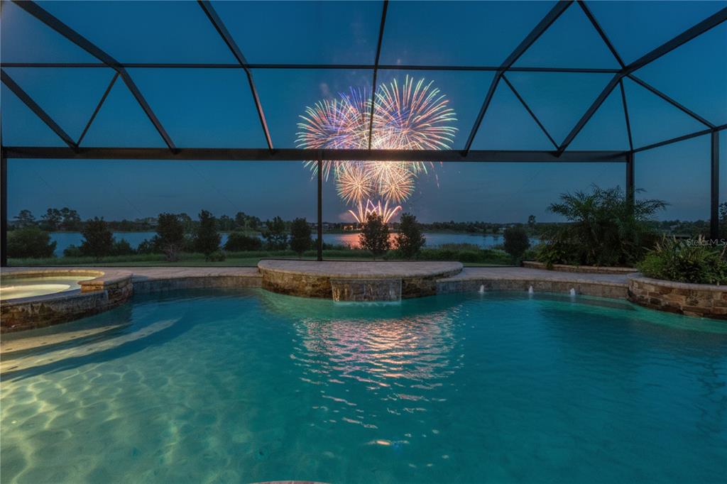 A swimming pool with a waterfall feature overlooks a lake under a fireworks display — 9969 LOST CREEK DRIVE, WINTER GARDEN, FL