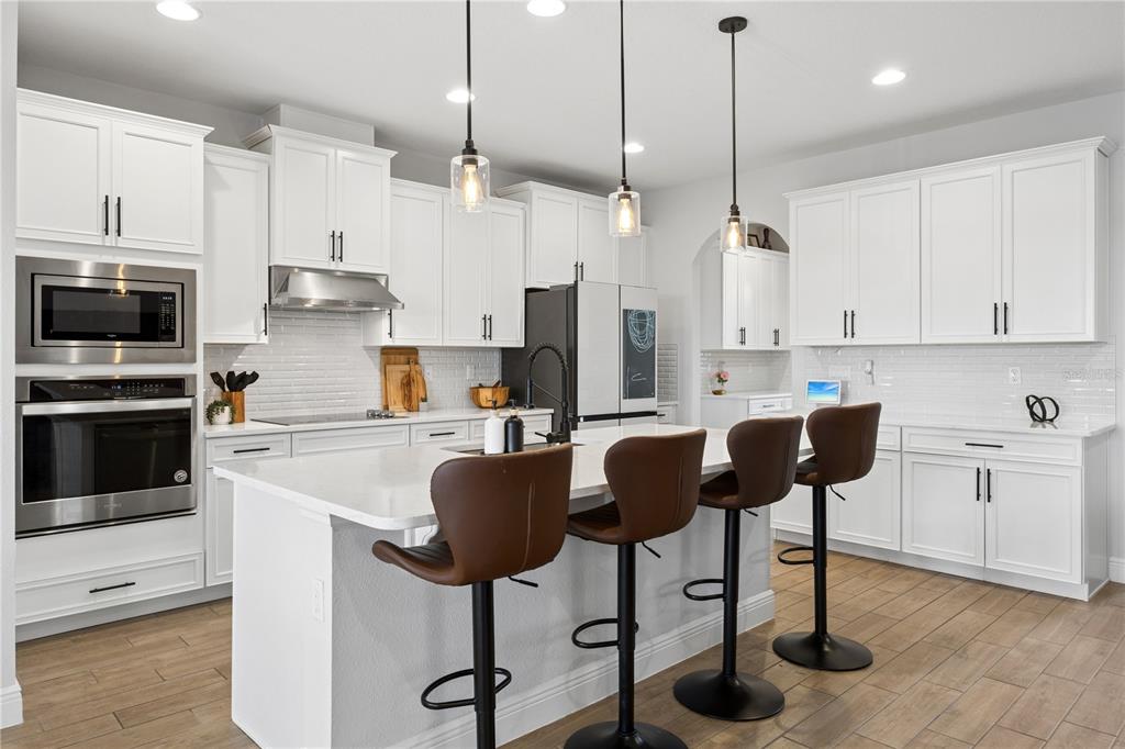 A modern kitchen features white cabinetry, a large island with bar stools, and stainless appliances — 9969 LOST CREEK DRIVE, WINTER GARDEN, FL