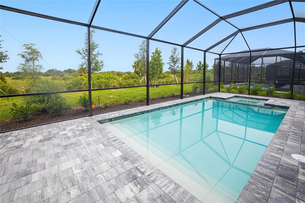 A screened-in patio features a rectangular swimming pool and an attached spa with stone pavers — 13314 GRASSMERE COURT, PUNTA GORDA, FL