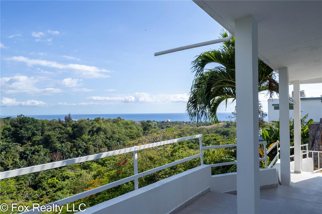 A two-story white house with a wrap-around balcony and metal railings sits among lush greenery — 412 INT CARR BO PUEBLO, RINCON, PR