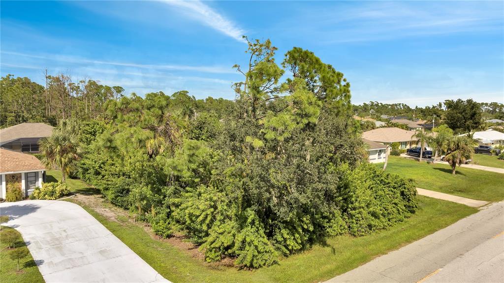 A vacant, tree-covered residential lot is situated between two houses along a paved street — 18042 LAKE WORTH BOULEVARD, PORT CHARLOTTE, FL
