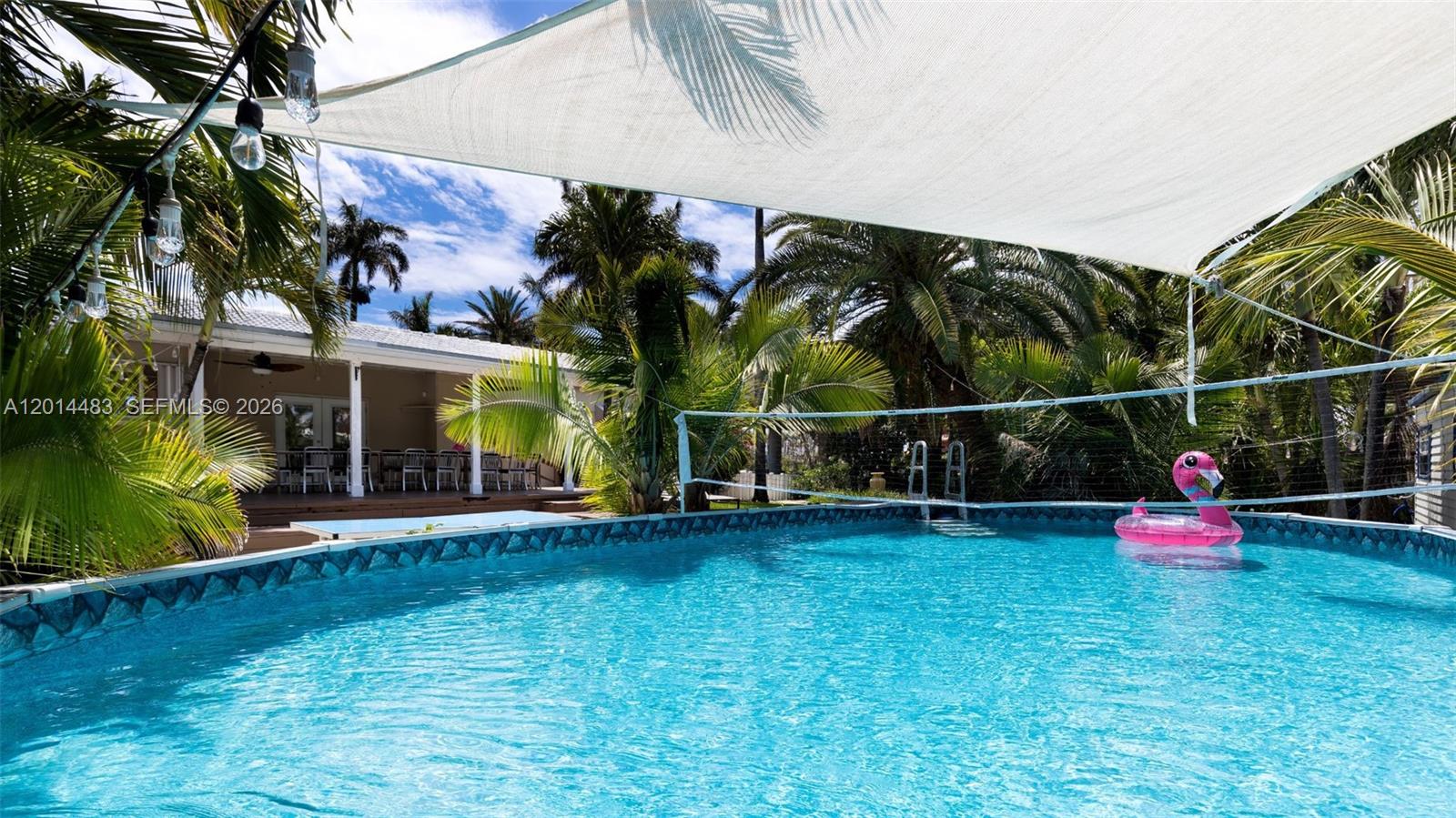 A swimming pool with a volleyball net and a pink flamingo float under a shade sail — 701 Hollywood Blvd, Hollywood FL 33019, HOLLYWOOD, FL