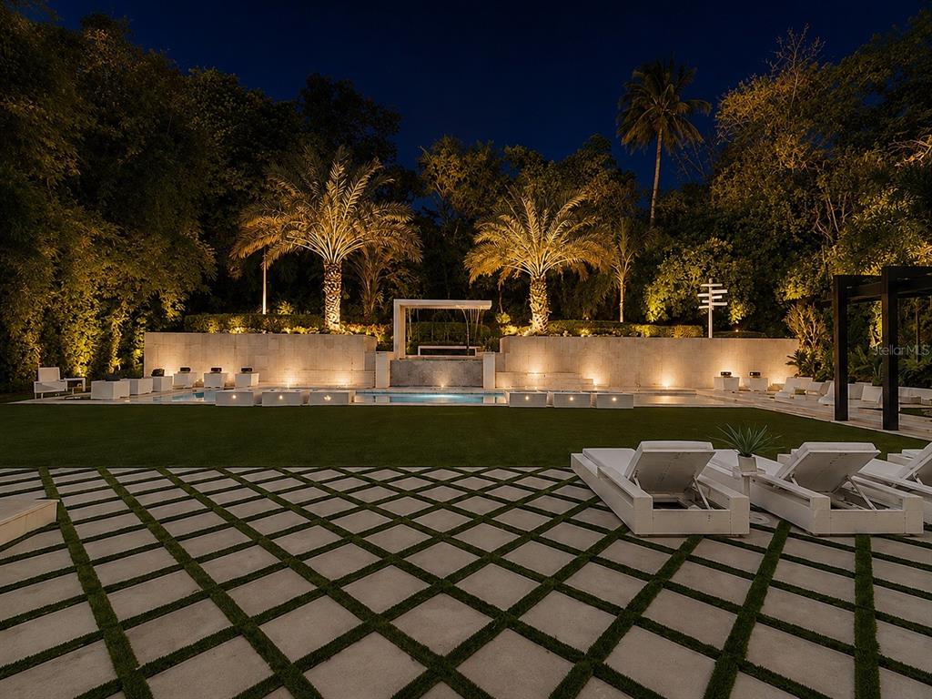 A modern backyard at night features a swimming pool, stone wall, palm trees, and patio — 276 DORADO BEACH EAST, DORADO, PR