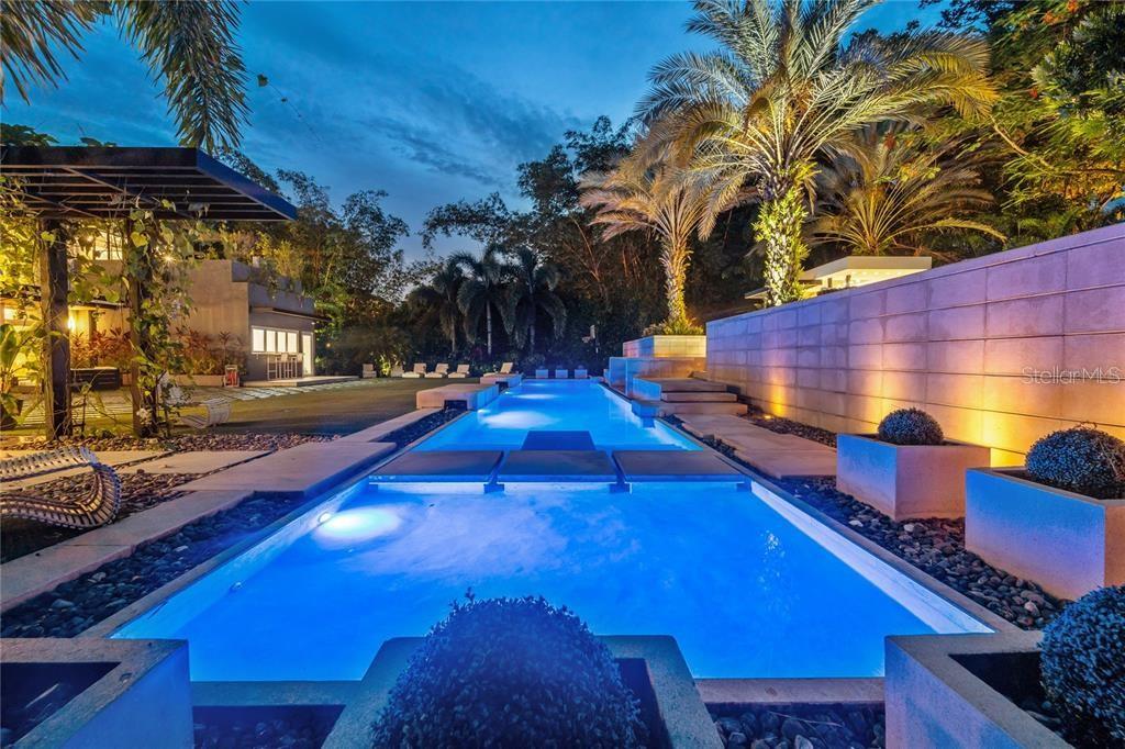 A long, illuminated rectangular swimming pool sits in a landscaped backyard at twilight — 276 DORADO BEACH EAST, DORADO, PR