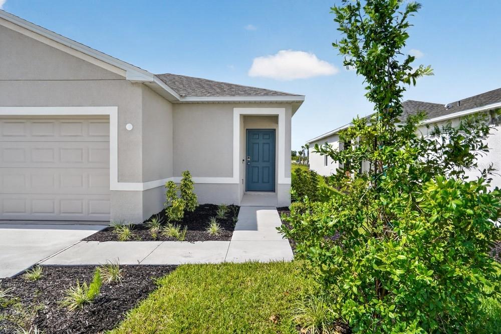 A single-story house exterior with a gray garage, blue front door, and landscaped front yard — 13411 CAMELOT COURT, PARRISH, FL