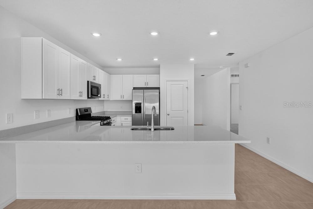 A modern kitchen features white cabinets, stainless steel appliances, and a large quartz island — 13411 CAMELOT COURT, PARRISH, FL