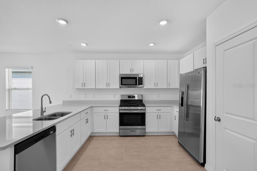 A modern kitchen features white cabinets, stainless steel appliances, and light-colored countertops — 13411 CAMELOT COURT, PARRISH, FL