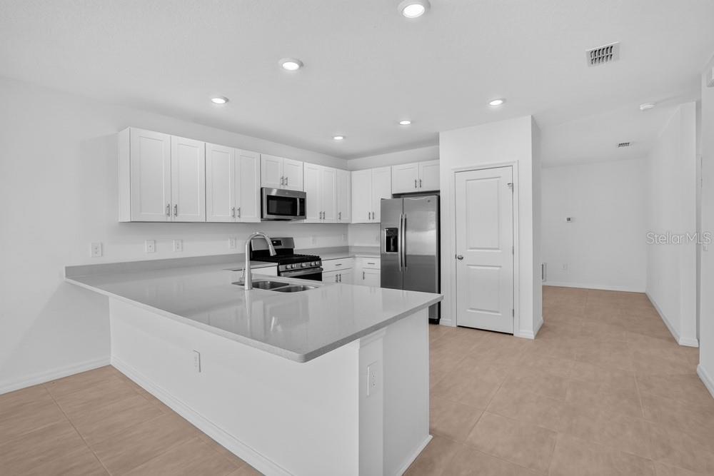 A modern kitchen features white cabinets, stainless steel appliances, and a large gray island countertop — 13411 CAMELOT COURT, PARRISH, FL