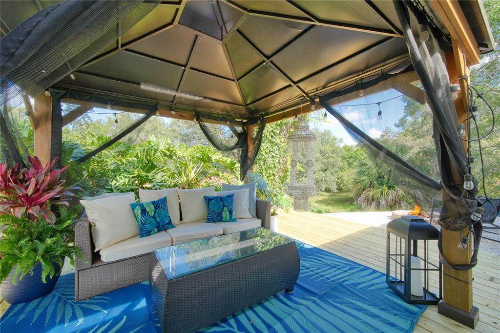 A covered outdoor patio features a wicker sofa, glass-topped coffee table, and a blue rug — 2751 WILSON COURT, PALM HARBOR, FL