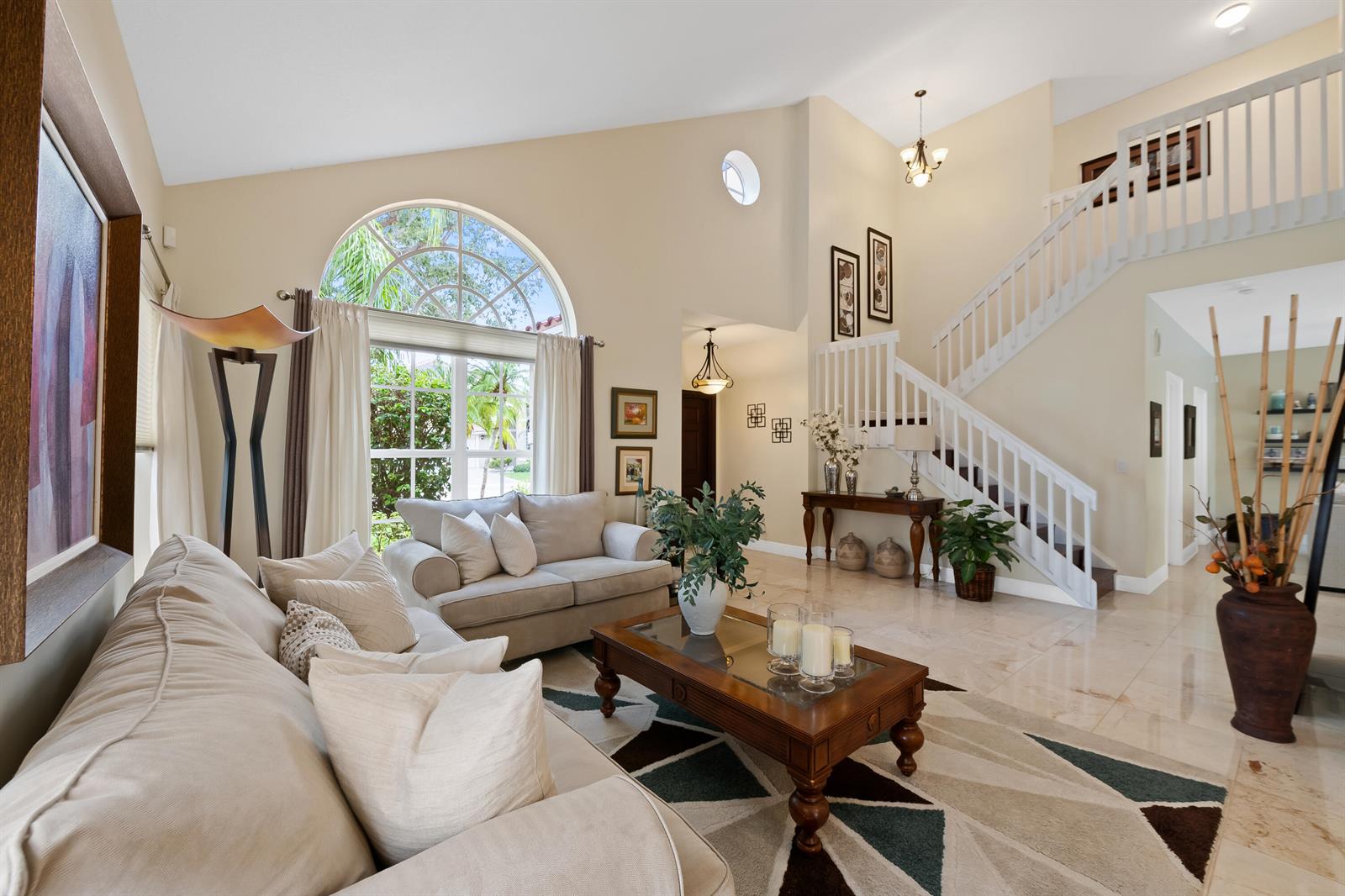 A bright living room features a vaulted ceiling, arched window, staircase, and tile flooring — 10927 La Salinas Circle, Boca Raton FL 33428, BOCA RATON, FL