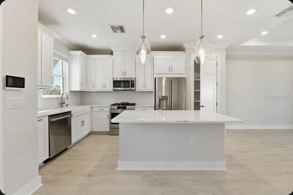A modern kitchen features white cabinetry, stainless steel appliances, a center island, and light flooring — 4052 SANTA CATERINA BOULEVARD UNIT 10102, BRADENTON, FL