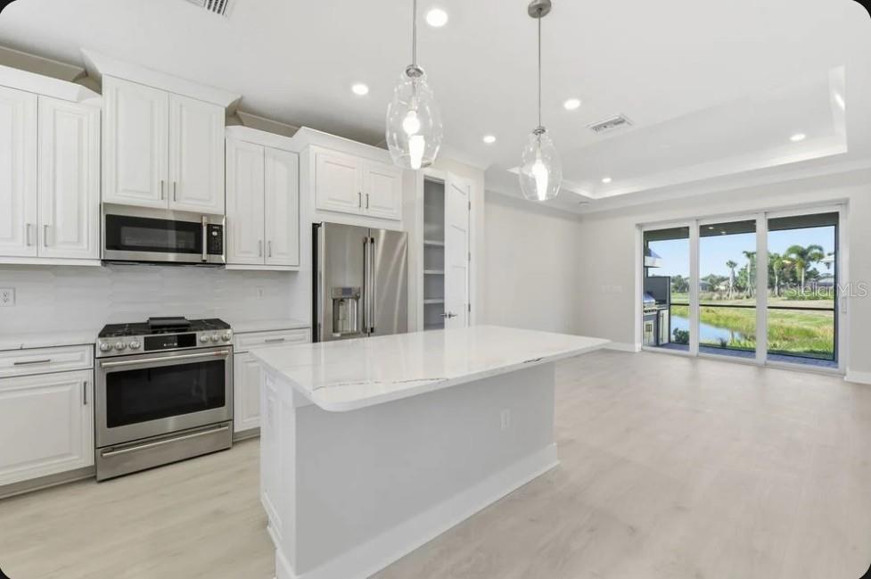 A modern white kitchen features stainless steel appliances, a quartz island, and sliding glass doors — 4052 SANTA CATERINA BOULEVARD UNIT 10102, BRADENTON, FL