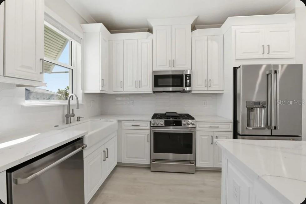 A kitchen features white cabinets, stainless steel appliances, a farmhouse sink, and white countertops — 4052 SANTA CATERINA BOULEVARD UNIT 10102, BRADENTON, FL