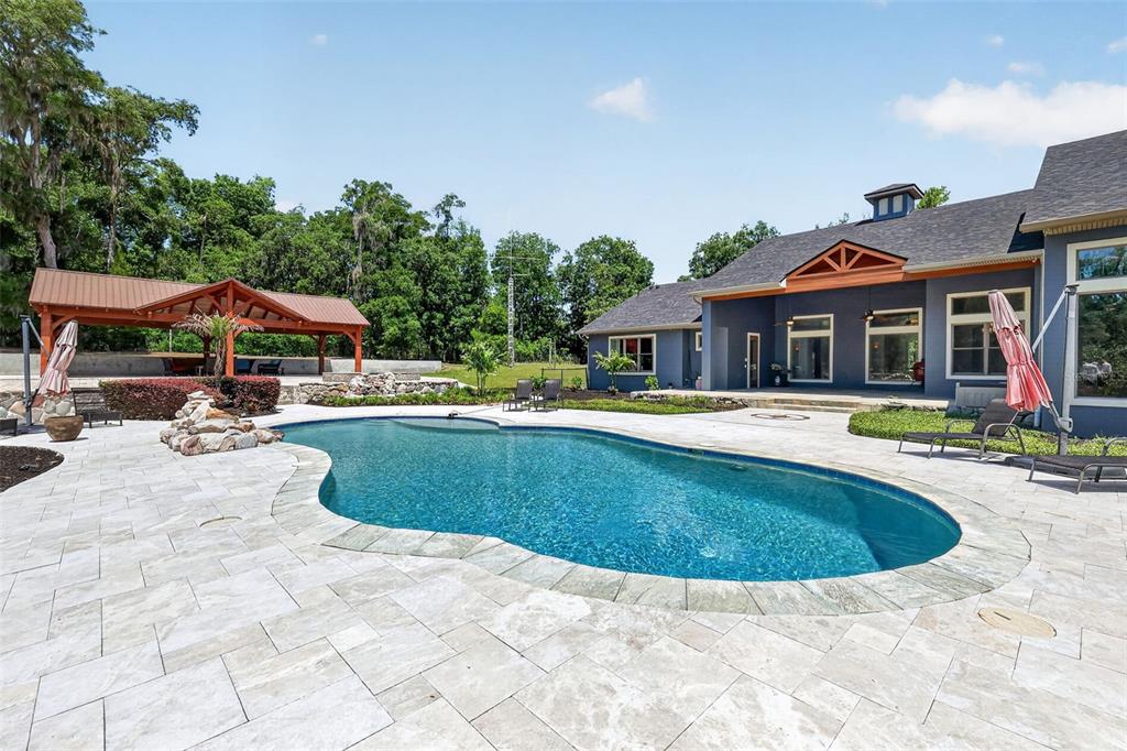 A backyard features a swimming pool, stone patio, and a covered pavilion near a house — 2110 HIGHLAND PARK ROAD, DELAND, FL