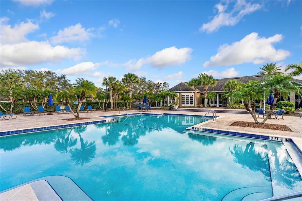 A swimming pool with blue water and depth markers sits in front of a clubhouse — 8933 MANOR LOOP UNIT 104, BRADENTON, FL