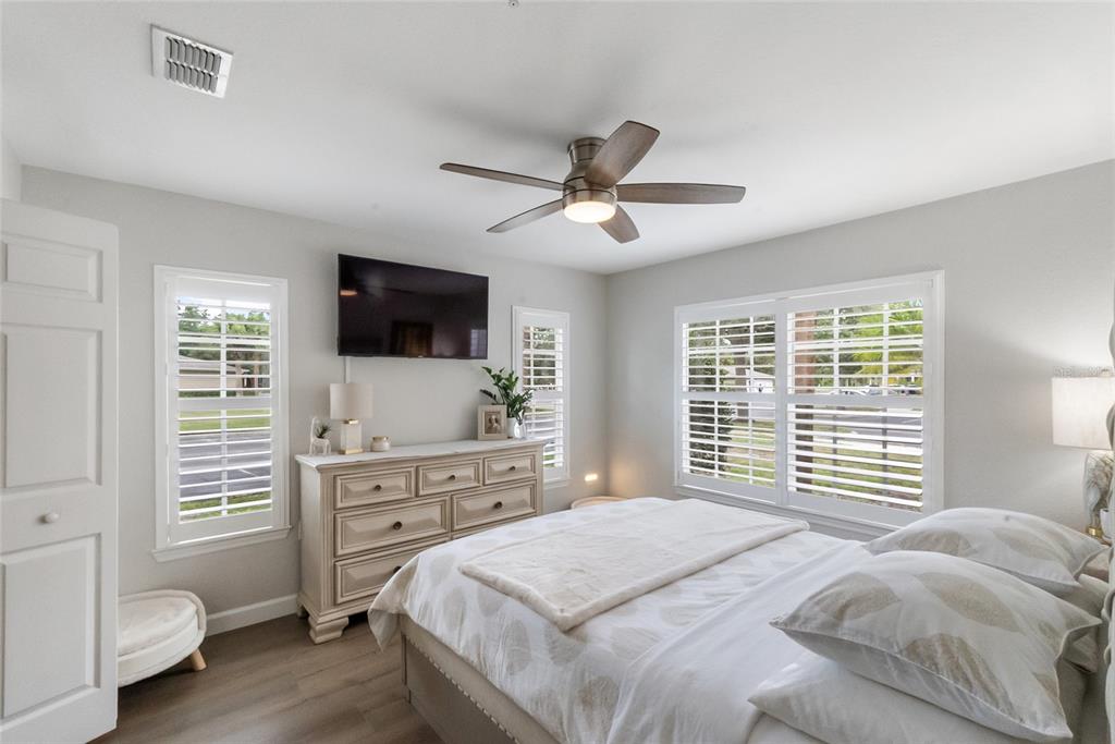 A bedroom features a bed, a dresser with a television, and windows with white shutters — 8933 MANOR LOOP UNIT 104, BRADENTON, FL