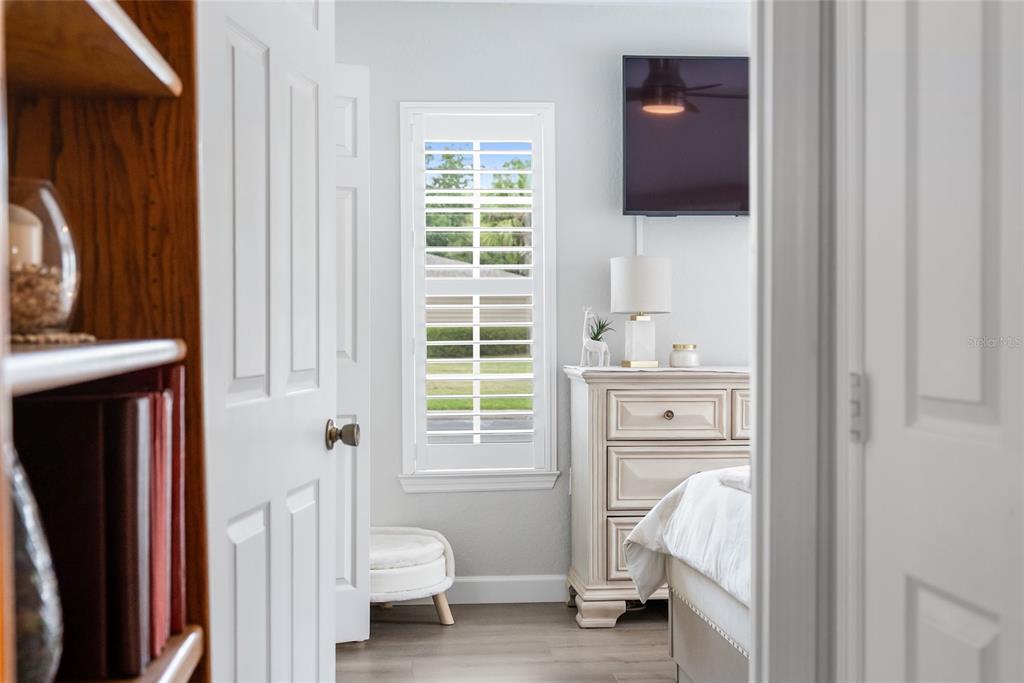 A view through a doorway shows a bedroom with a dresser, television, and window shutters — 8933 MANOR LOOP UNIT 104, BRADENTON, FL