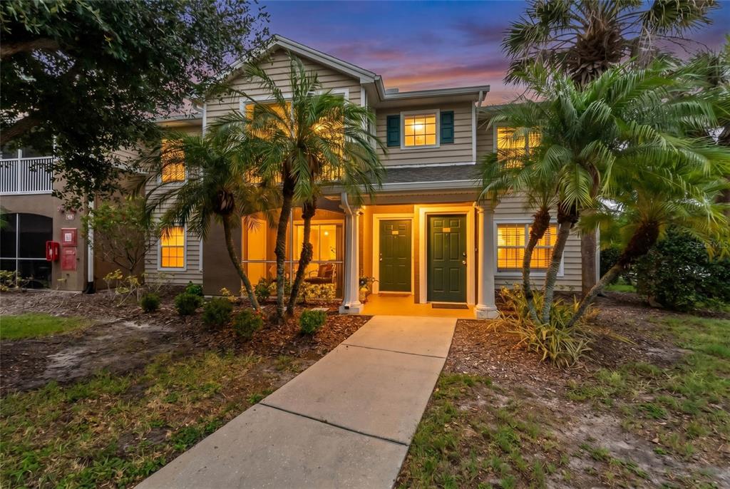 A two-story tan building features a concrete walkway leading to two green front doors — 8933 MANOR LOOP UNIT 104, BRADENTON, FL