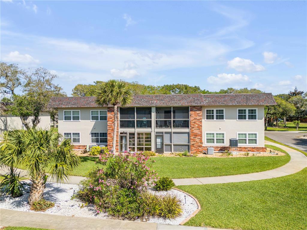 A two-story apartment building with a brick facade, screened balconies, and a landscaped front yard — 3800 SAXON DRIVE UNIT A7, NEW SMYRNA BEACH, FL