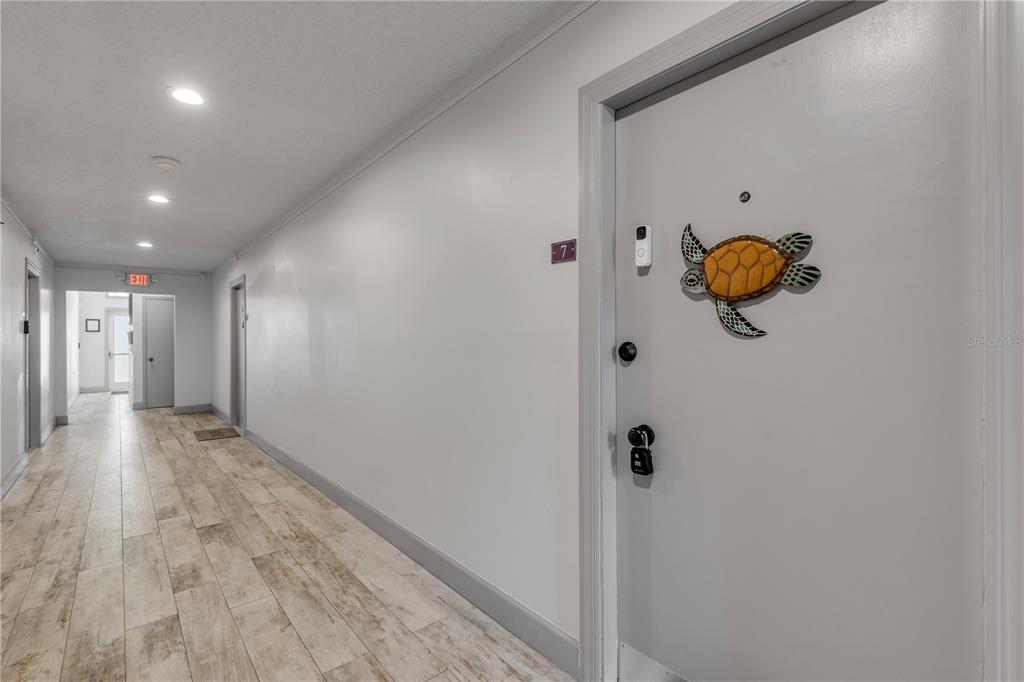 A hallway with light wood-look tile flooring leads toward an exit door — 3800 SAXON DRIVE UNIT A7, NEW SMYRNA BEACH, FL