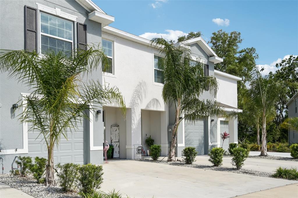 A two-story townhouse exterior features gray and white stucco walls, palm trees, and concrete driveways — 16646 MAUDE DRIVE, WIMAUMA, FL