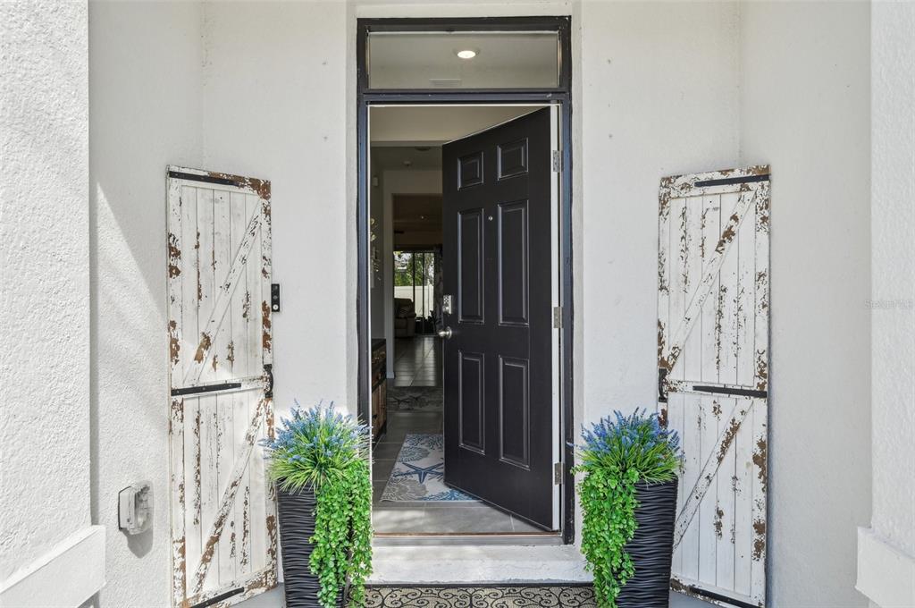 An open black front door is flanked by two rustic white shutters and potted plants — 16646 MAUDE DRIVE, WIMAUMA, FL