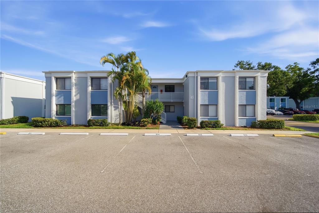 A two-story apartment building features a light gray exterior with blue accents and parking spaces — 5310 26TH STREET W UNIT 304, BRADENTON, FL