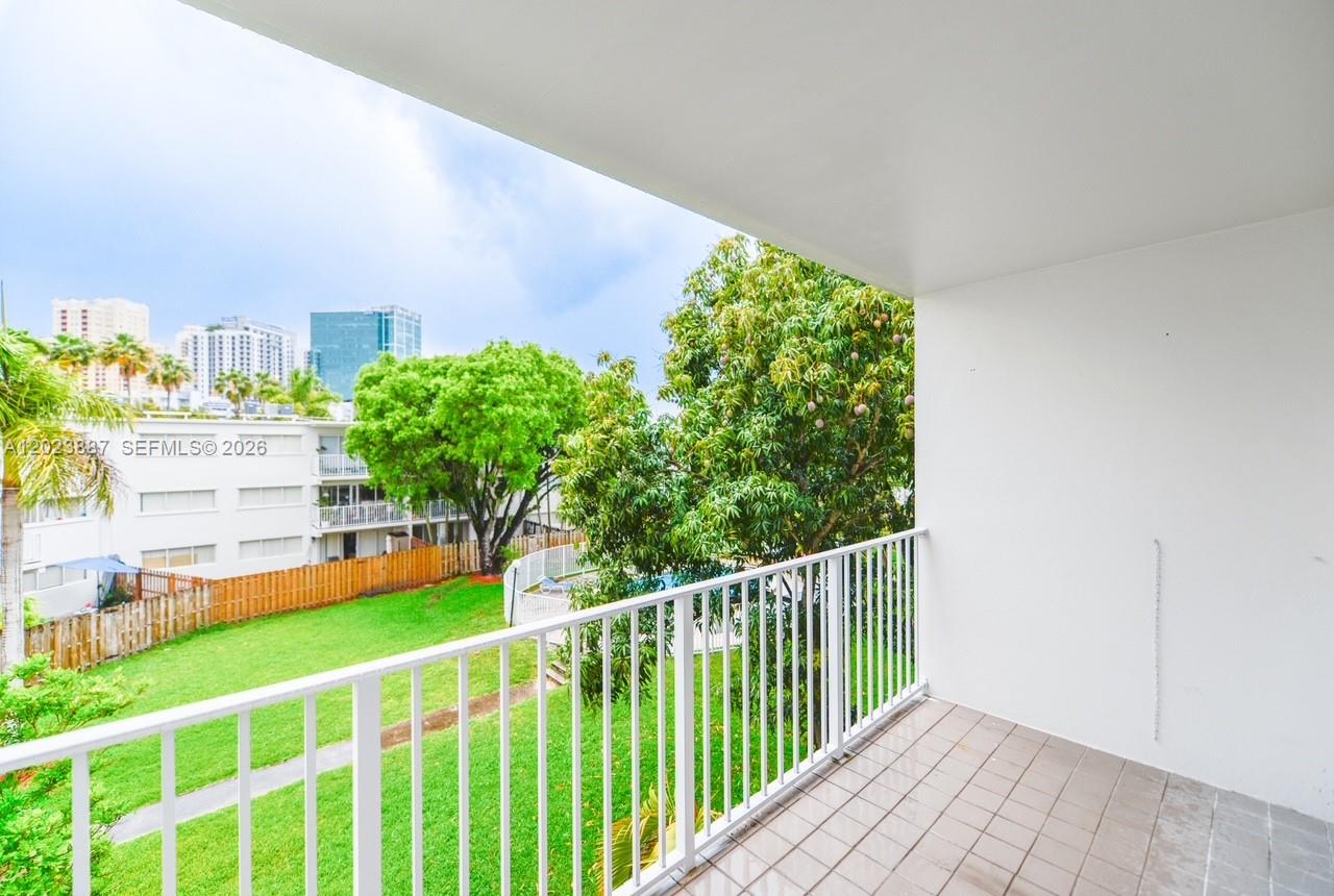 A balcony with white railings overlooks a grassy courtyard, trees, and distant city buildings — 7737 SW 88th St # C312, Miami FL 33156, MIAMI, FL