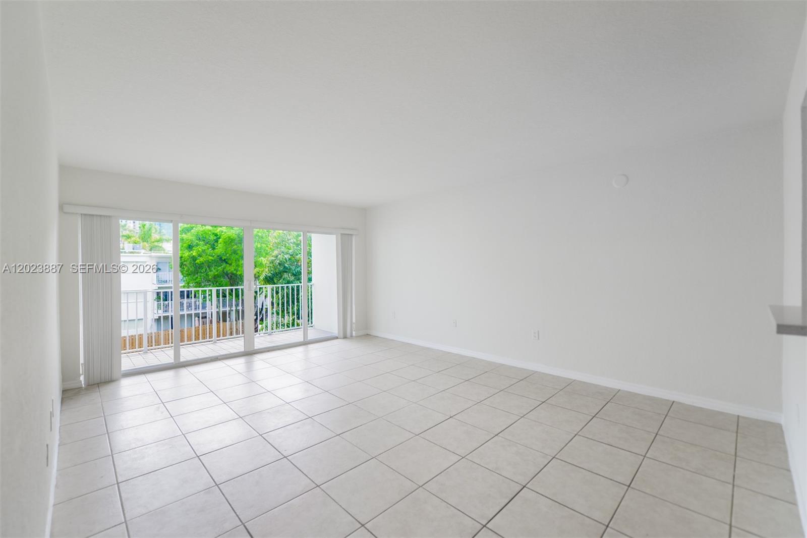 An empty living room features white walls, light tile flooring, and a sliding glass door — 7737 SW 88th St # C312, Miami FL 33156, MIAMI, FL