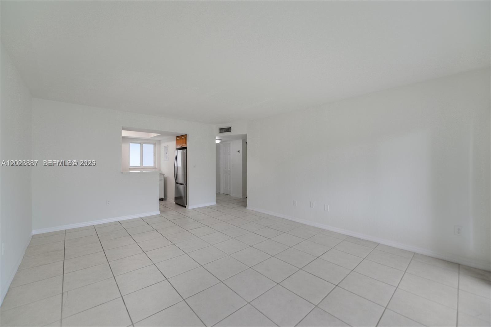 An empty living room features white walls, light-colored tile flooring, and an open kitchen pass-through — 7737 SW 88th St # C312, Miami FL 33156, MIAMI, FL