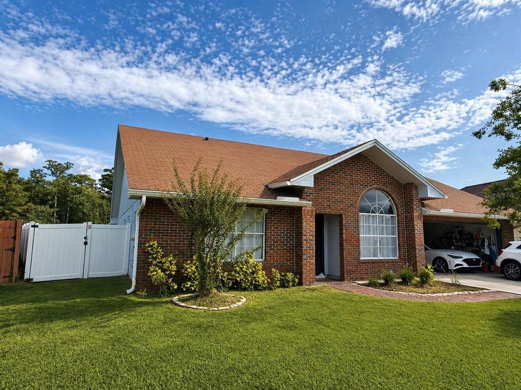 A single-story brick house with a brown shingled roof, arched window, and attached garage — 1927 GAMBOGE DRIVE, ORLANDO, FL