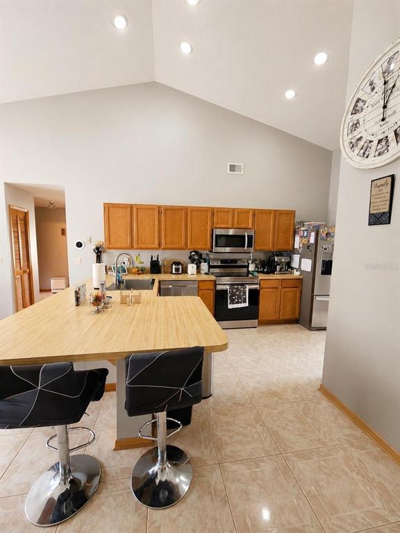 A kitchen with light wood cabinets, a large island, and tile flooring under a vaulted ceiling — 1927 GAMBOGE DRIVE, ORLANDO, FL