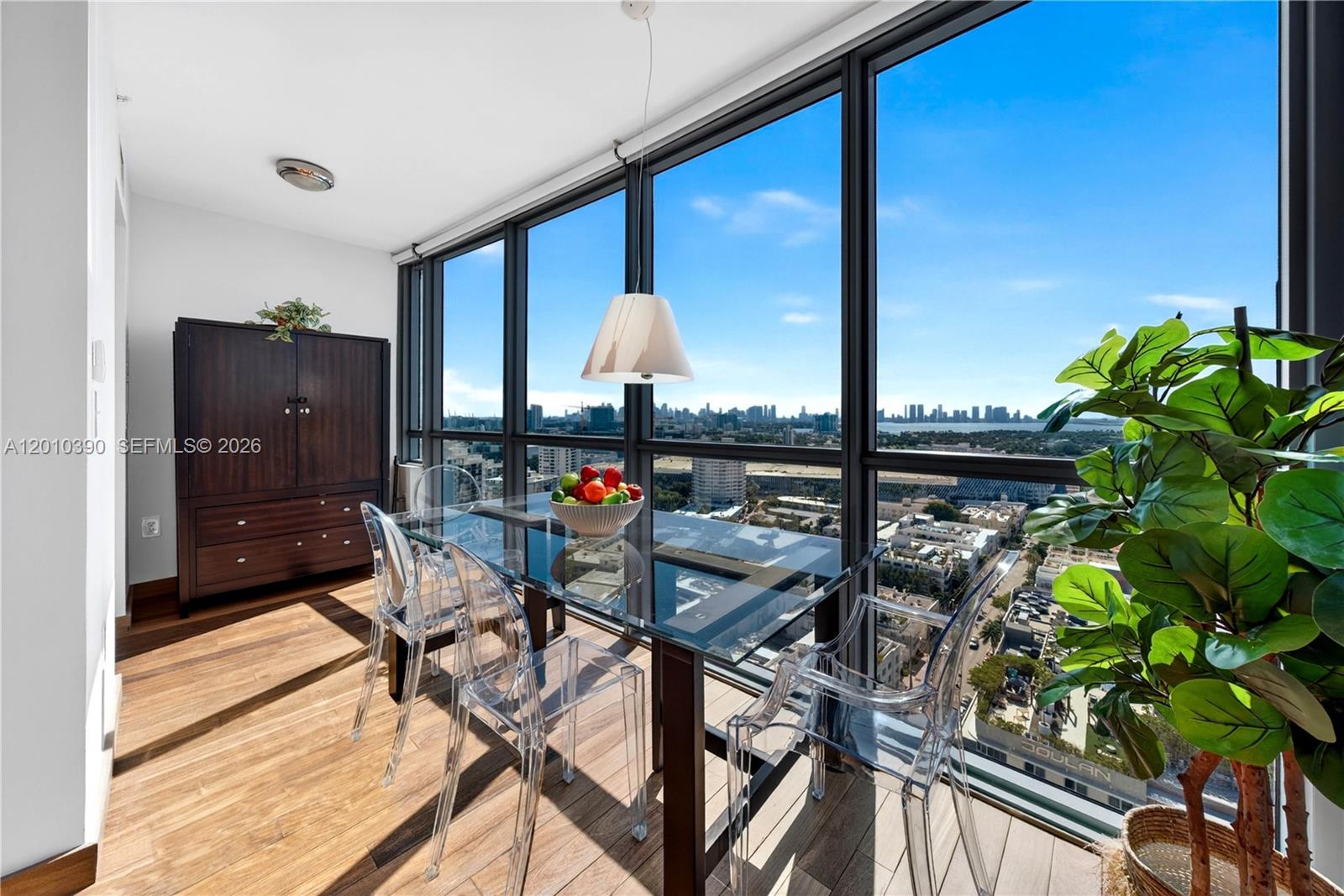 A dining area features a glass table, transparent chairs, and floor-to-ceiling windows overlooking a city — 101 20th St # 2601, Miami Beach FL 33139, MIAMI BEACH, FL
