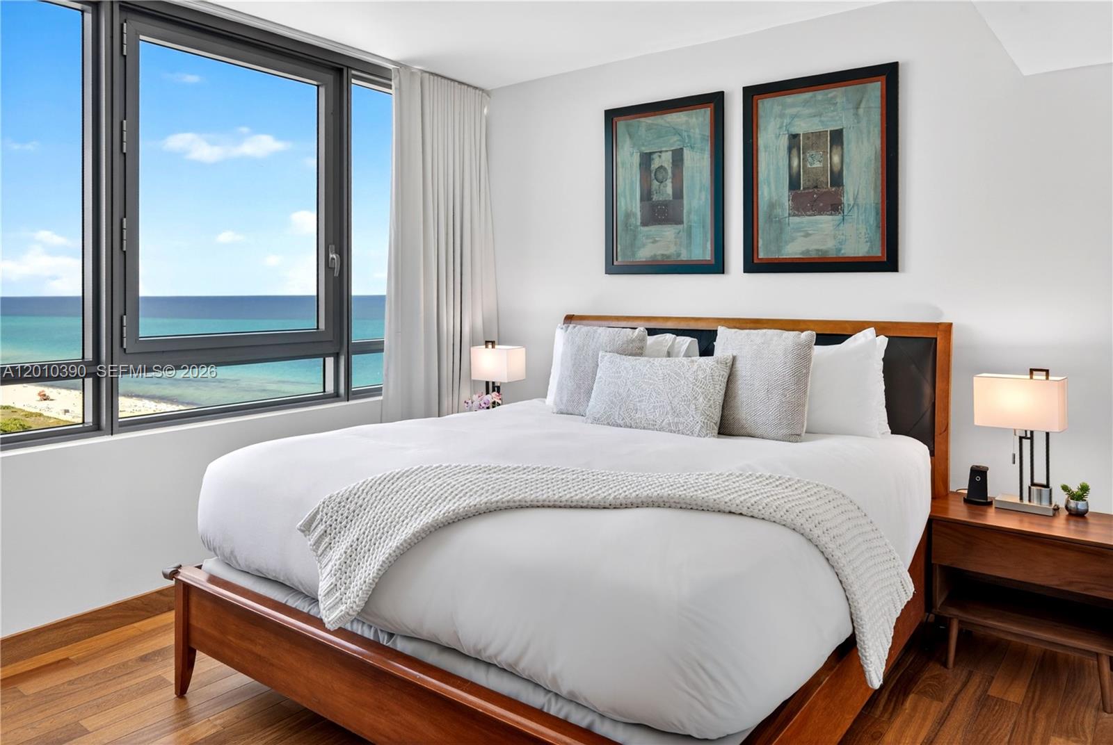 A bedroom features a wooden bed frame, white bedding, and a large window overlooking the ocean — 101 20th St # 2601, Miami Beach FL 33139, MIAMI BEACH, FL