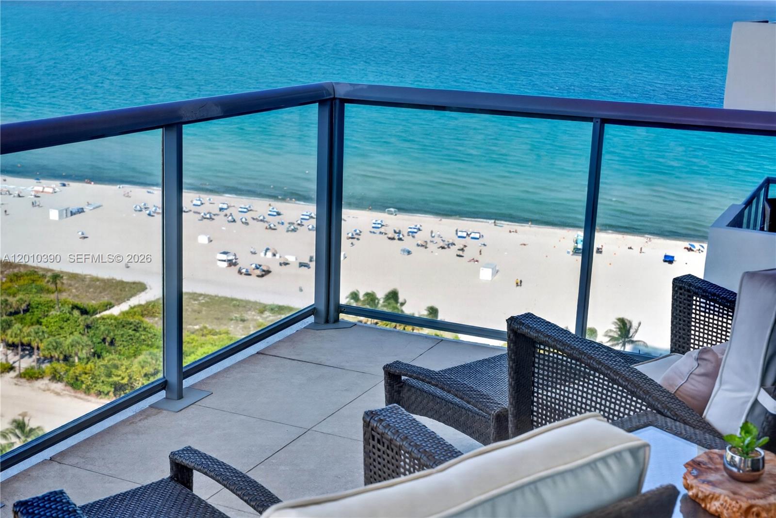 A balcony with wicker lounge chairs overlooks a sandy beach and the ocean — 101 20th St # 2601, Miami Beach FL 33139, MIAMI BEACH, FL