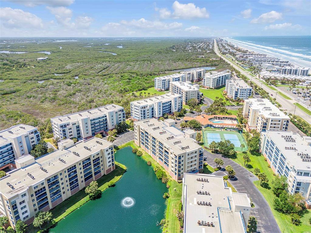 An aerial view of a coastal apartment complex with a pond and tennis court — 5300 S ATLANTIC AVENUE UNIT 8-206, NEW SMYRNA BEACH, FL