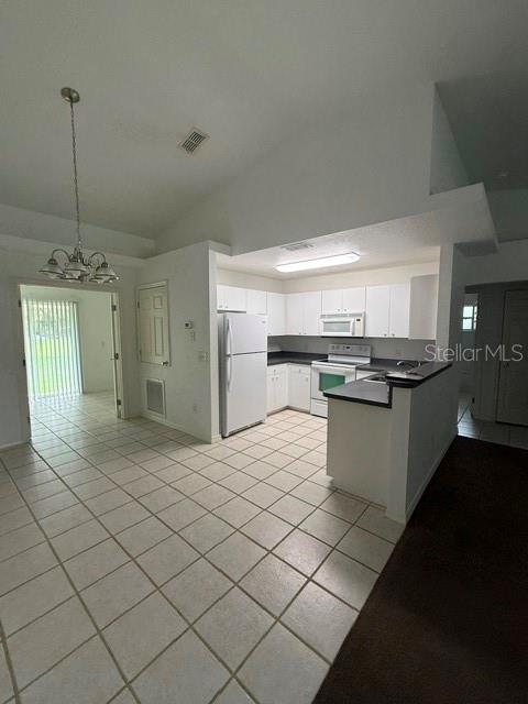 A kitchen with white cabinets and tile flooring opens to a dining area with a chandelier — 3100 SW 94TH STREET UNIT 2, OCALA, FL