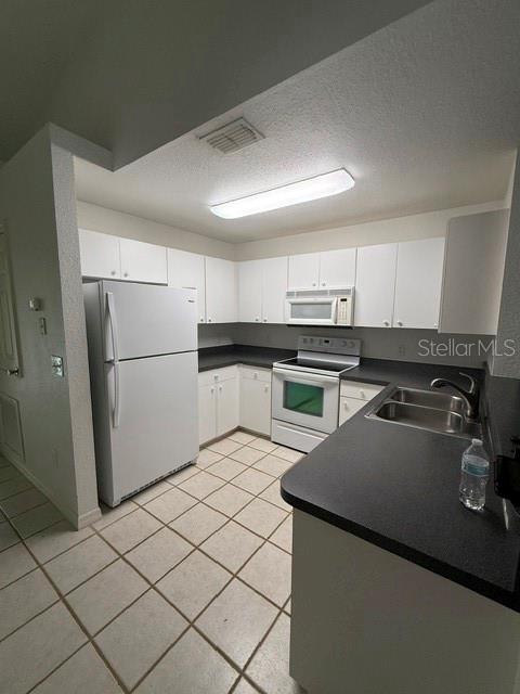 A kitchen with white cabinets, white appliances, dark countertops, and light-colored tile flooring — 3100 SW 94TH STREET UNIT 2, OCALA, FL