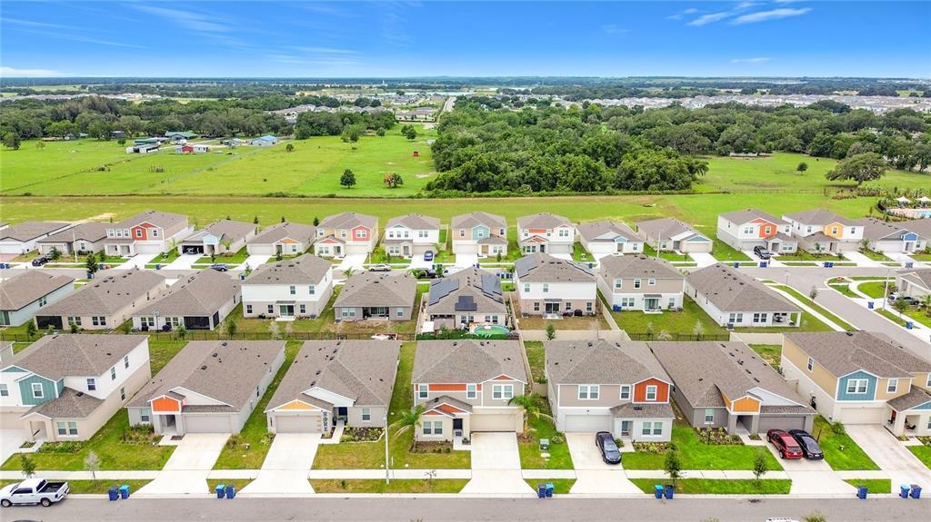 An aerial view shows a suburban neighborhood with rows of houses and a large field — 1414 SEA GLASS ROAD, HAINES CITY, FL