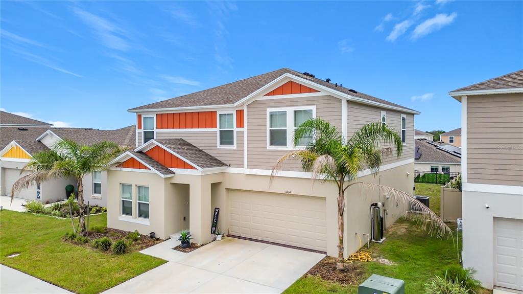 A two-story suburban house with tan siding, orange accents, and a two-car garage — 1414 SEA GLASS ROAD, HAINES CITY, FL