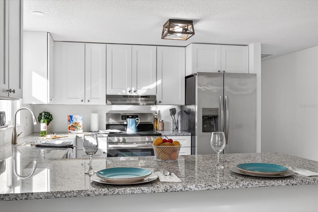 A kitchen features white cabinets, granite countertops, stainless steel appliances, and a breakfast bar — 4928 AMHERST COURT, NEW PORT RICHEY, FL