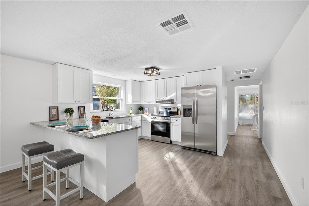 A kitchen features white cabinets, granite countertops, stainless steel appliances, and a breakfast bar — 4928 AMHERST COURT, NEW PORT RICHEY, FL