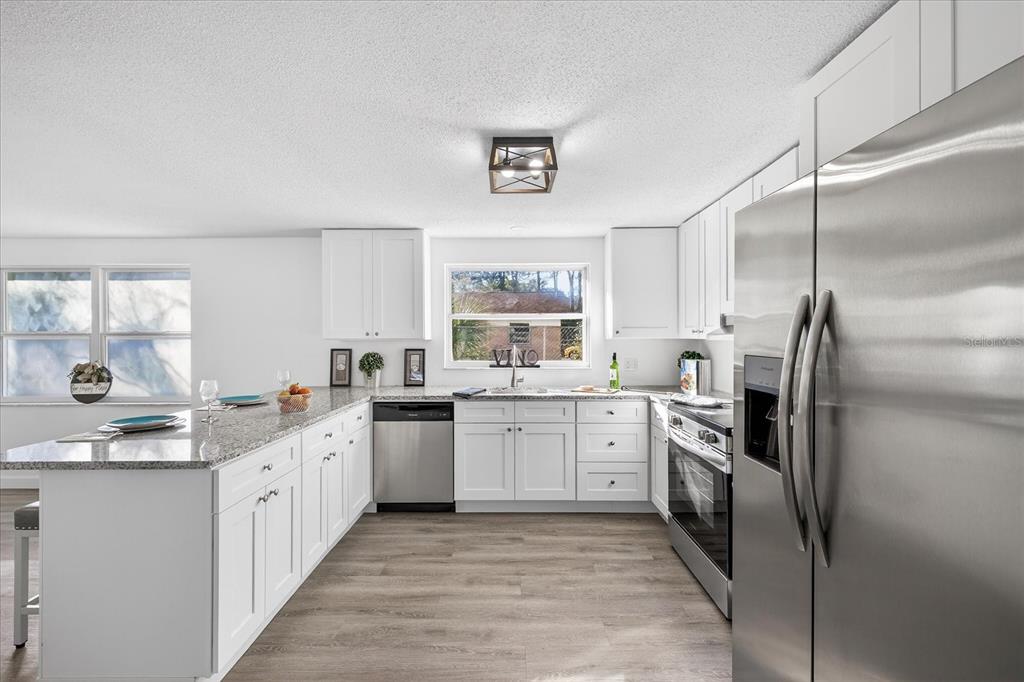 A modern kitchen features white cabinets, granite countertops, stainless steel appliances, and wood-look flooring — 4928 AMHERST COURT, NEW PORT RICHEY, FL